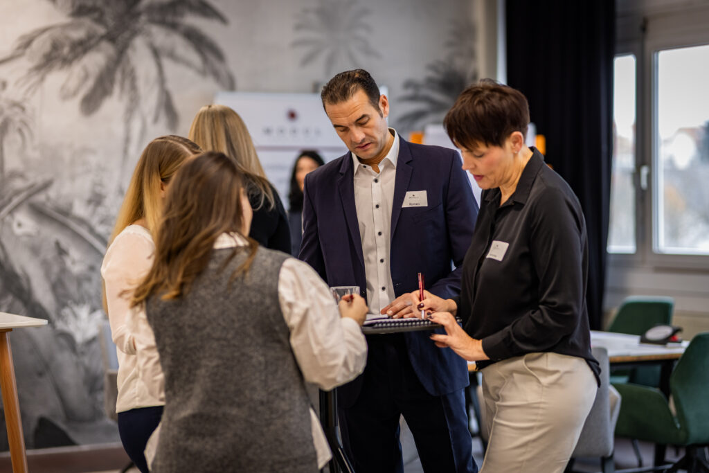 Führungskraft bespricht mit ihrem Team eine Aufgabe am Stehtisch im Seminarraum – MODUL TRAINING