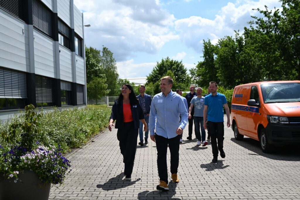 Service-Seminare: Seminarleitung geht mit einer Gruppe aus dem Handwerk über den Hof eines Betriebs, daneben ein Servicefahrzeug – MODUL TRAINING